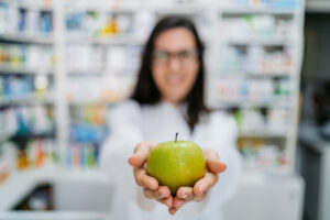 Young female pharmacist offering a green apple at the drug store.
